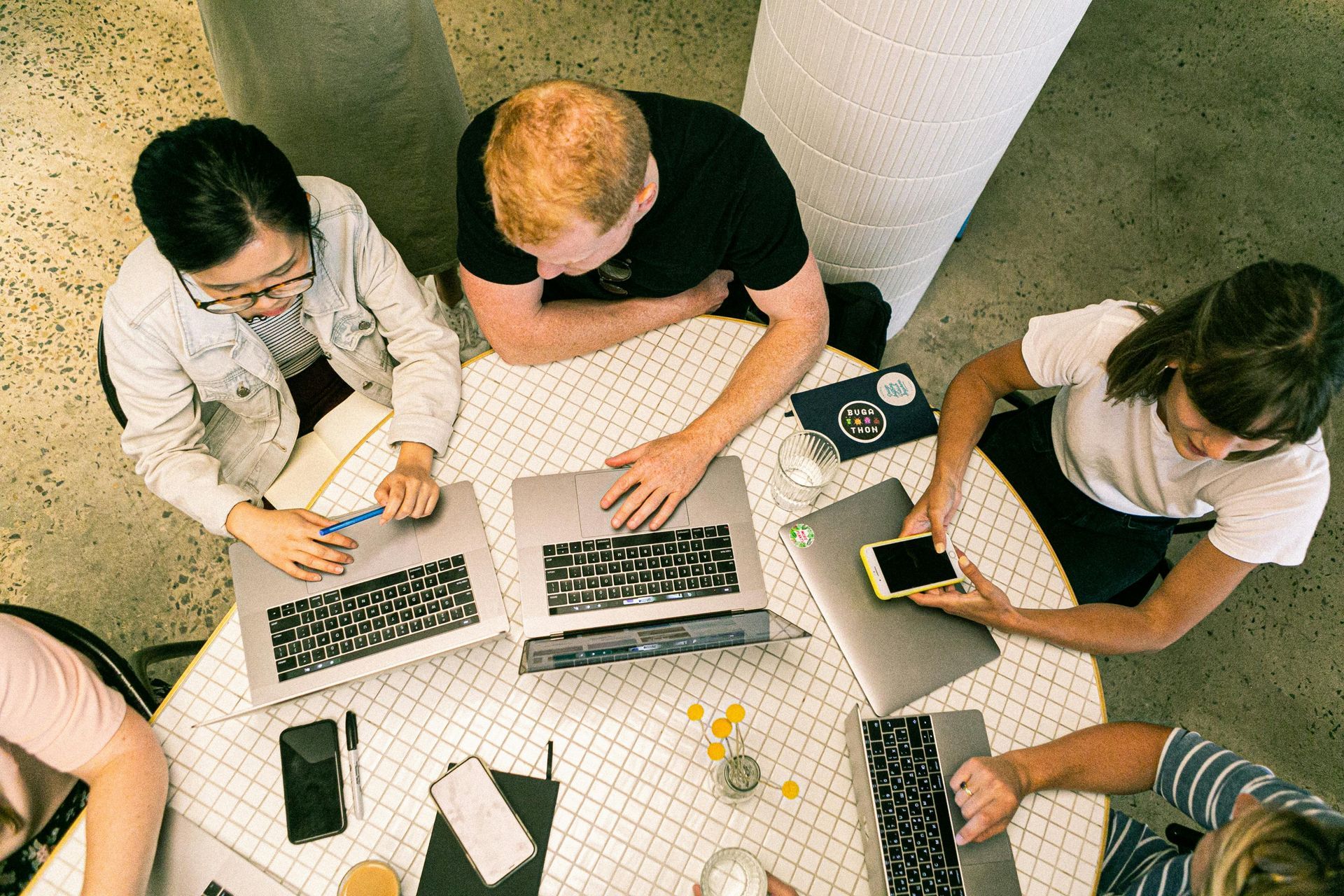 A group of people are sitting around a table with laptops. A group of people are sitting around a table with laptops.