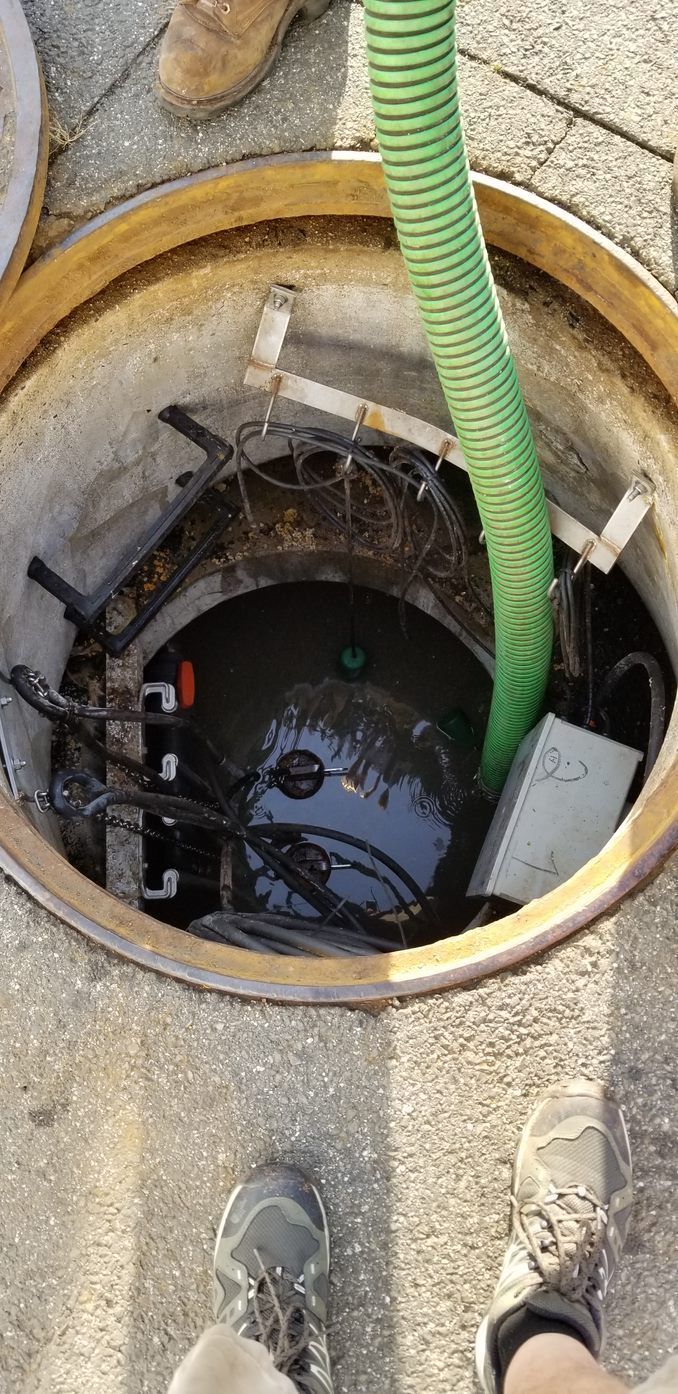 A person is pumping water into a manhole cover with a green hose.