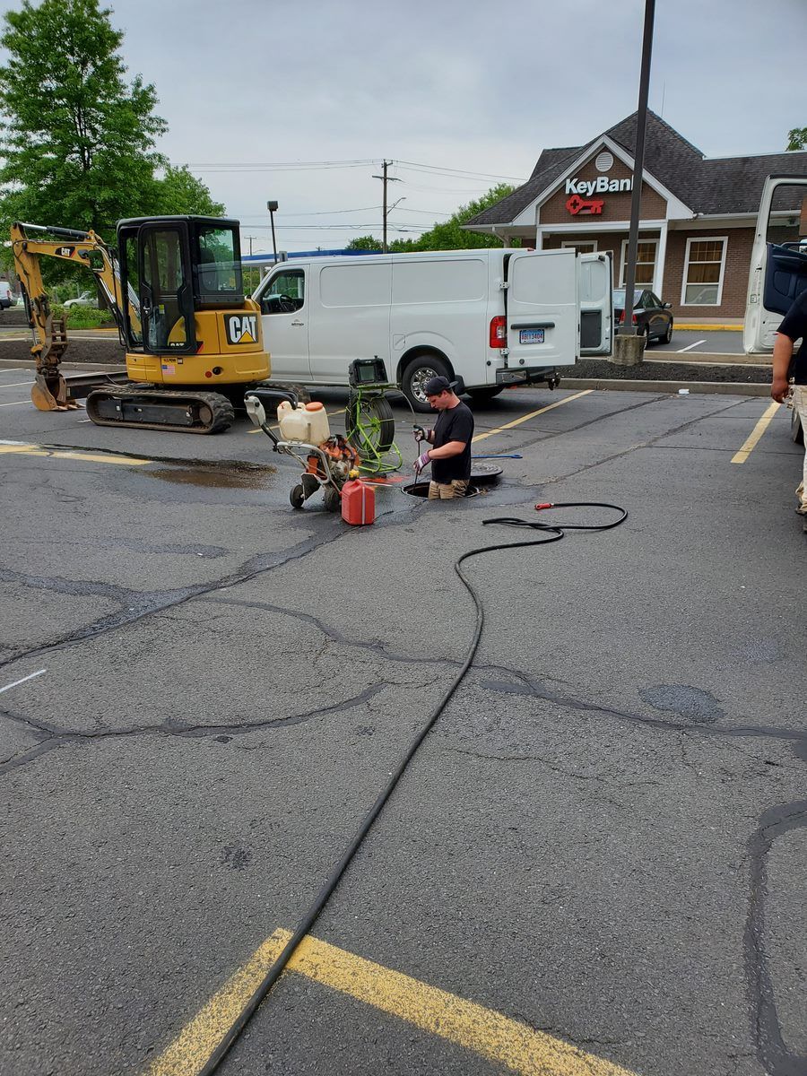 A man is kneeling in a parking lot next to a white van and a yellow excavator.