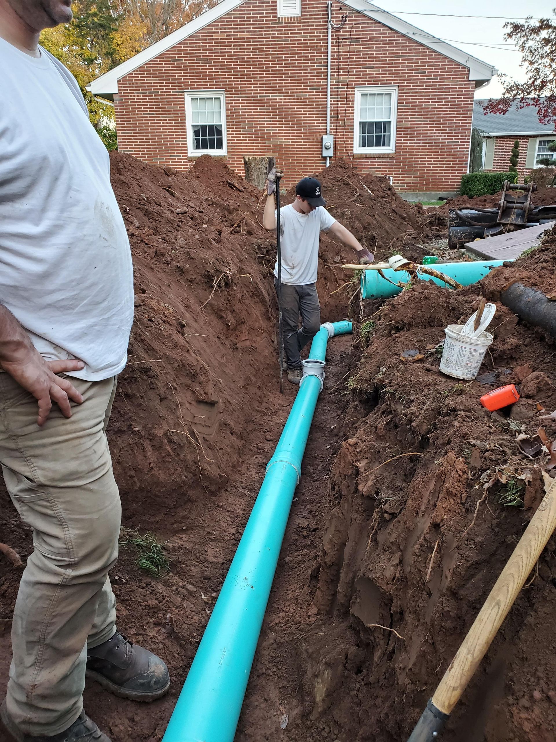 A man is standing next to a large green pipe in the dirt.