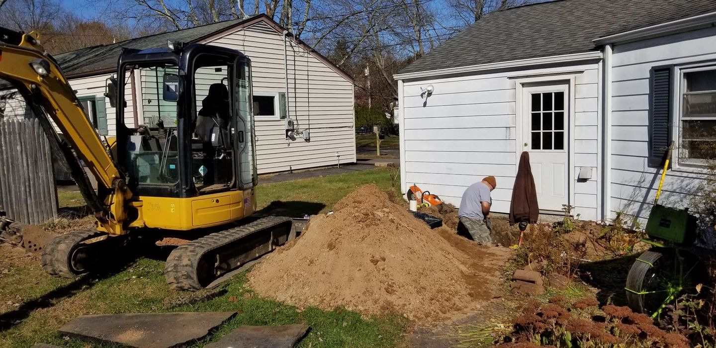 A yellow excavator is digging a hole in front of a house.