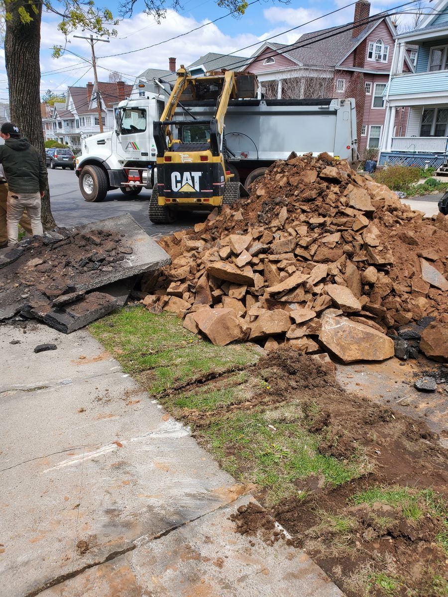 A dump truck is driving down a street next to a pile of rocks.