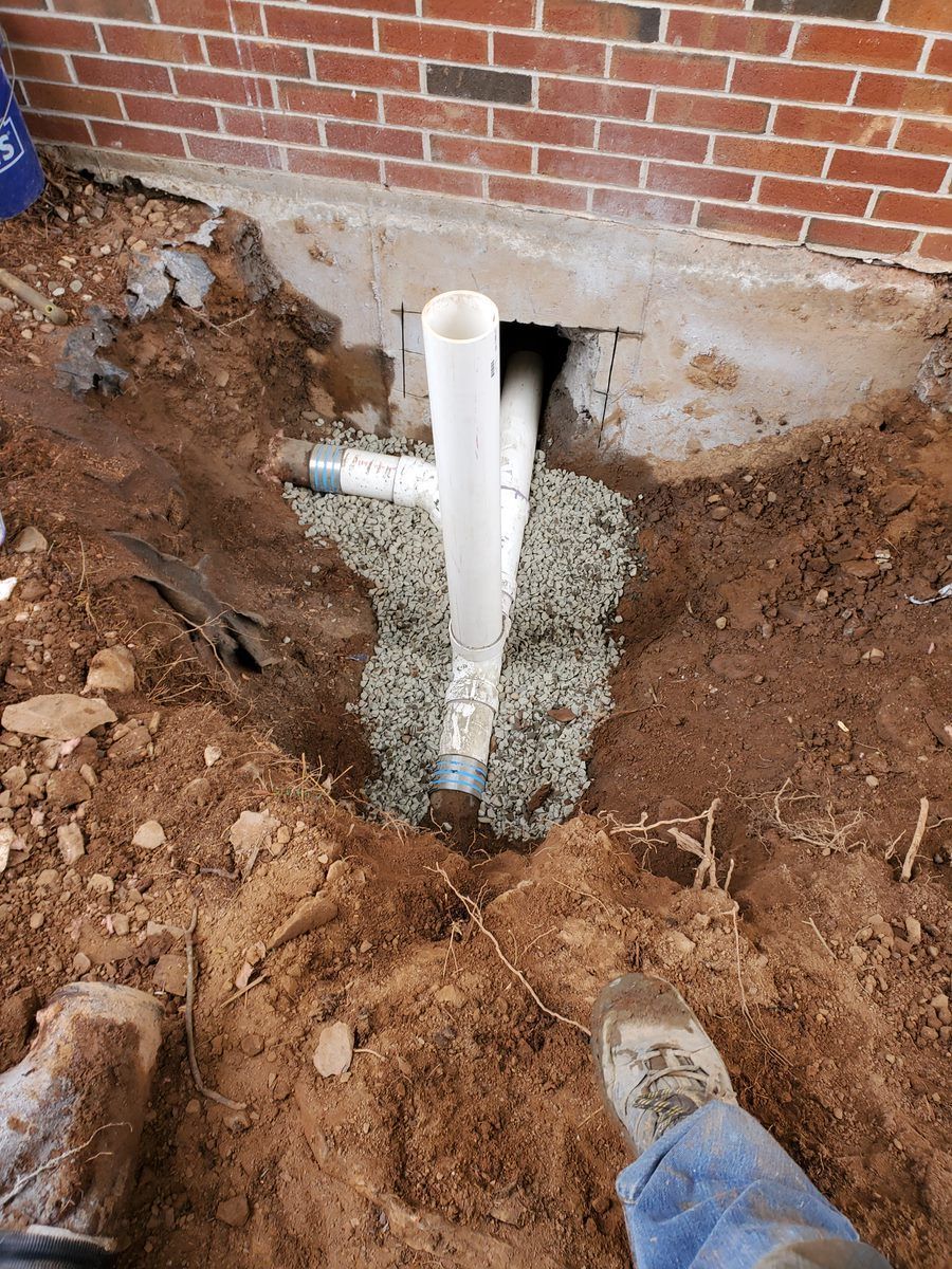 A person is standing in the dirt next to a drain pipe.
