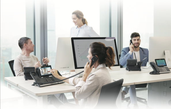 A group of people are sitting at desks in an office talking on phones.