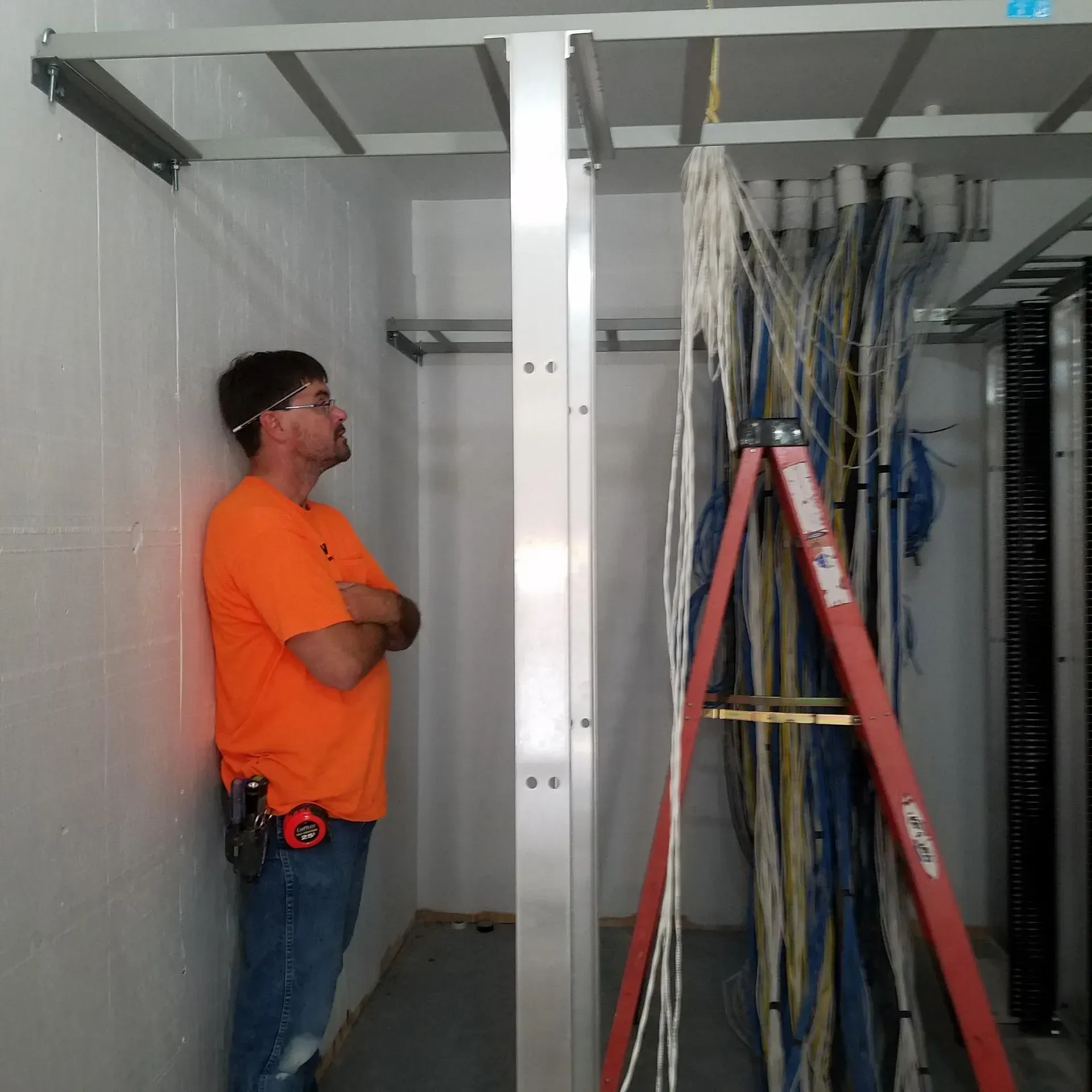 A man leaning against a wall next to a red ladder that says ' ridgid ' on it