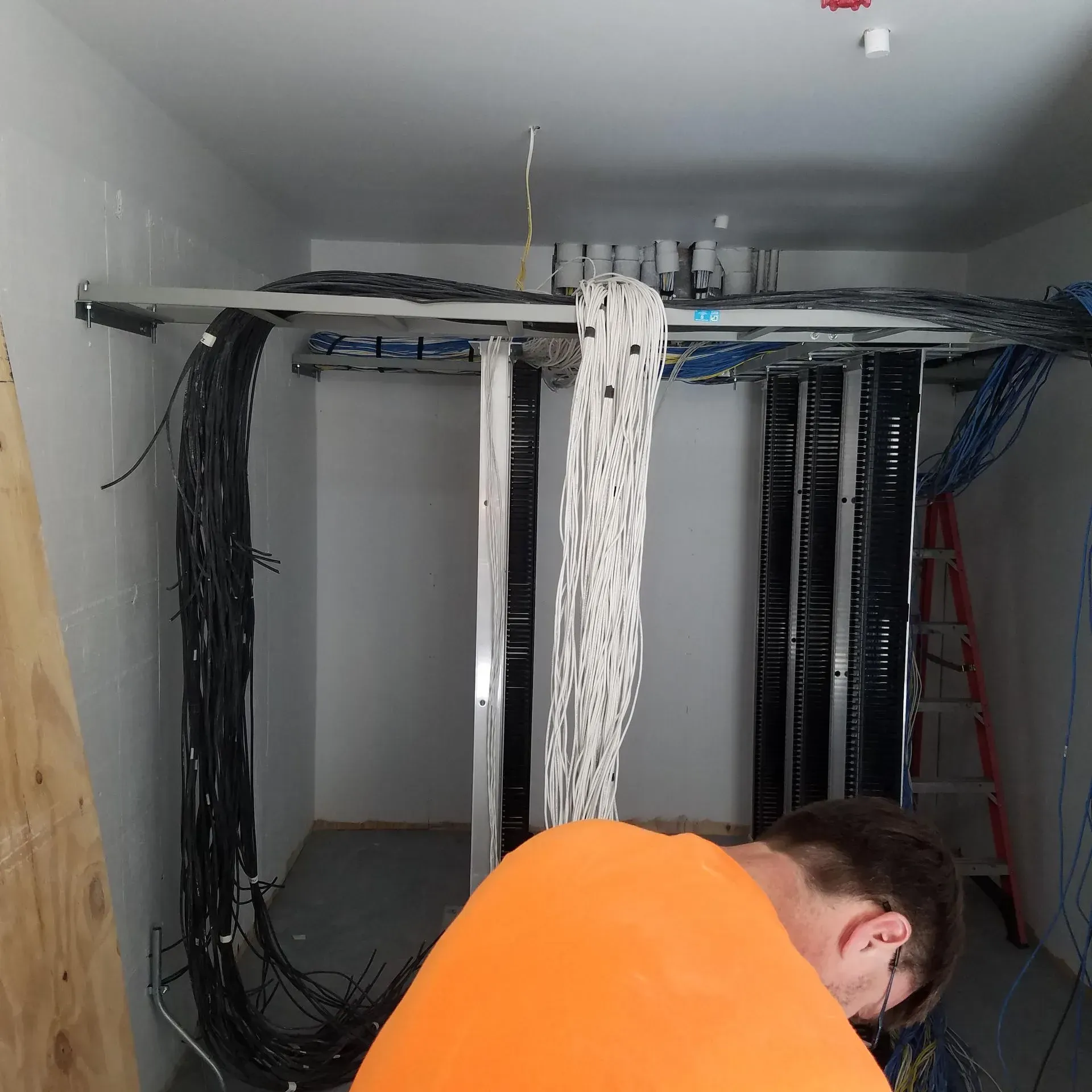 A man in an orange shirt is working in a server room
