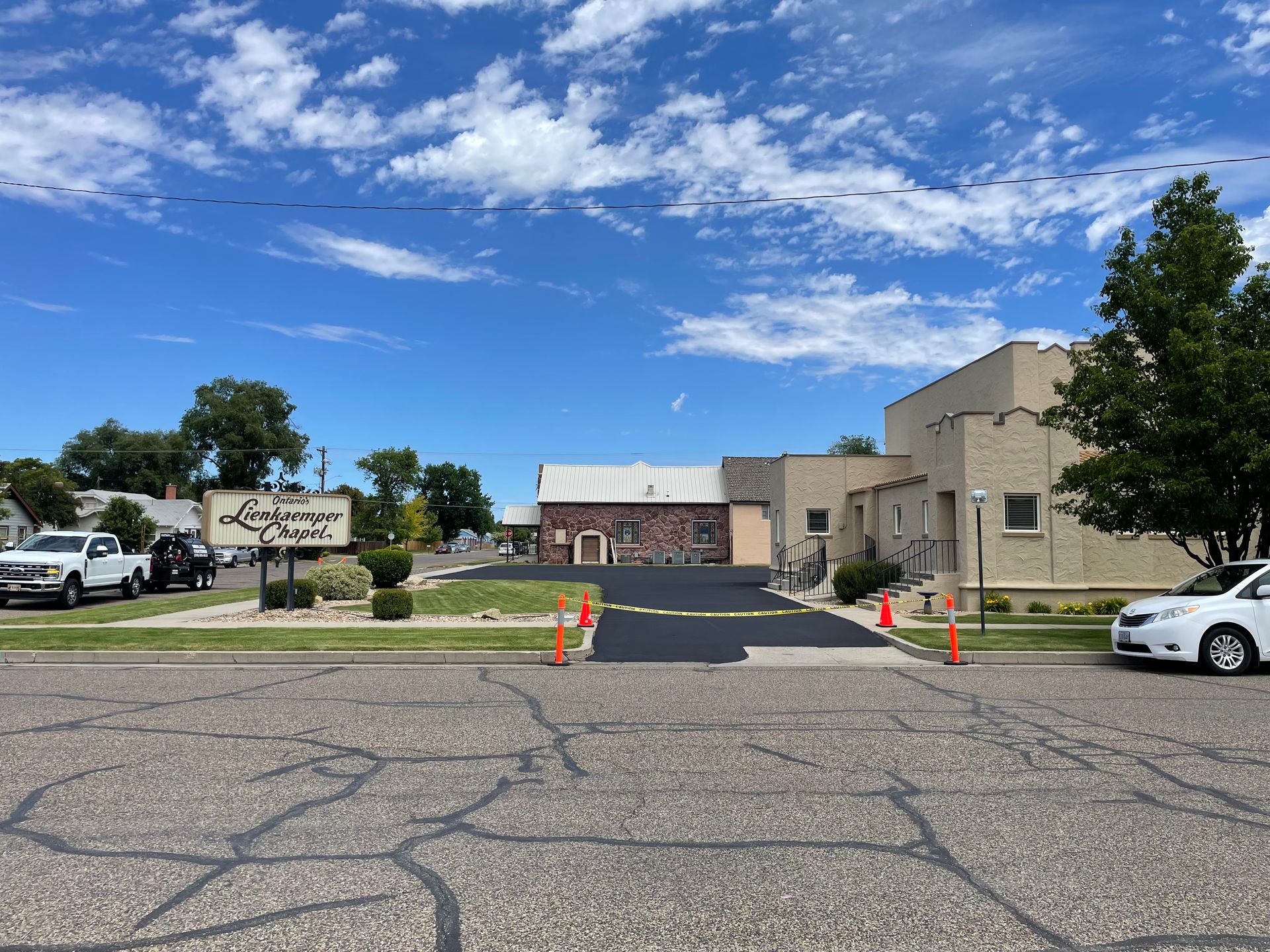 A sunny view of a small building with a newly paved driveway and a sign reading 