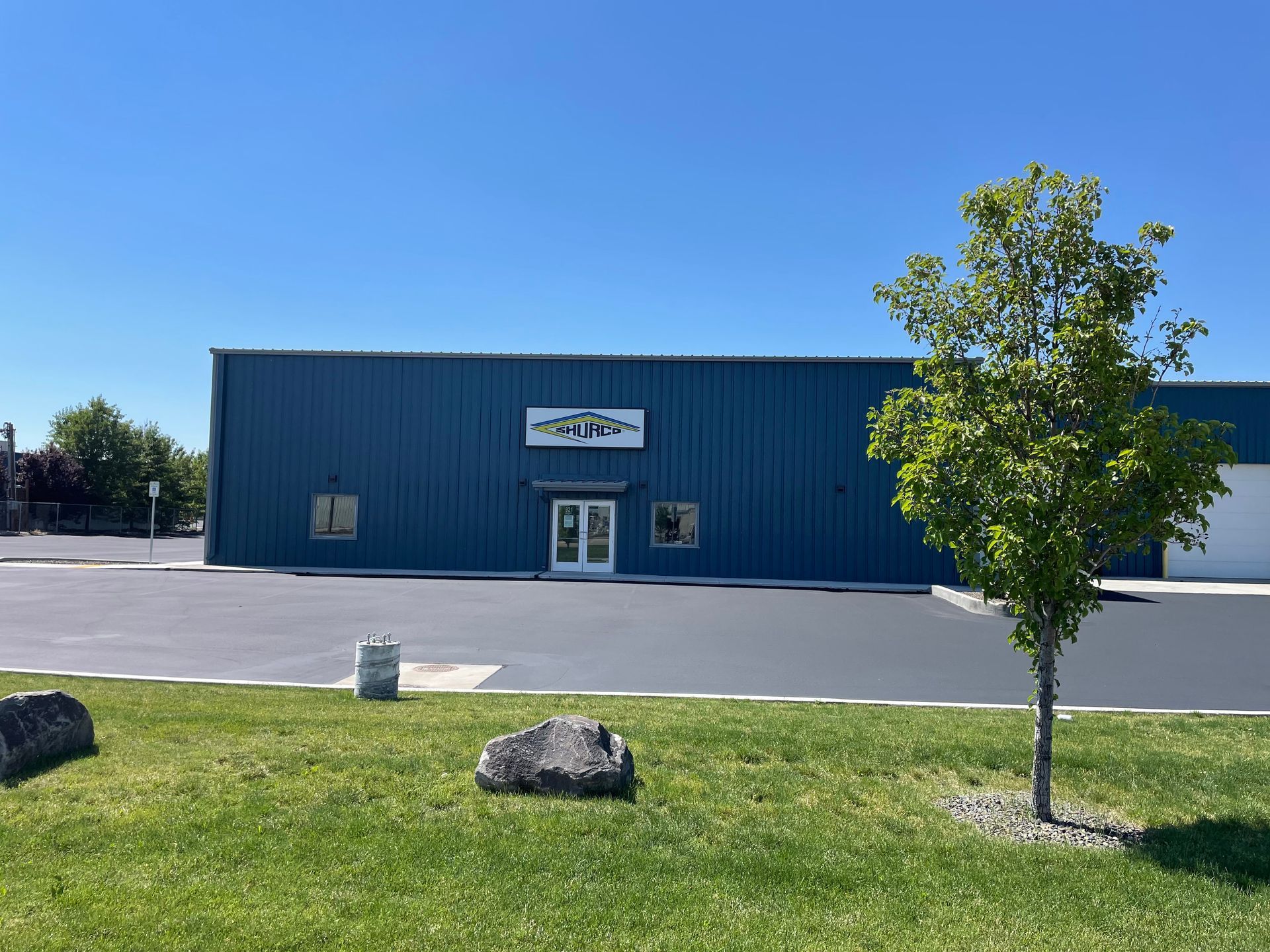 A blue, single-story metal commercial building with a central entrance and parking lot, set under a clear blue sky.