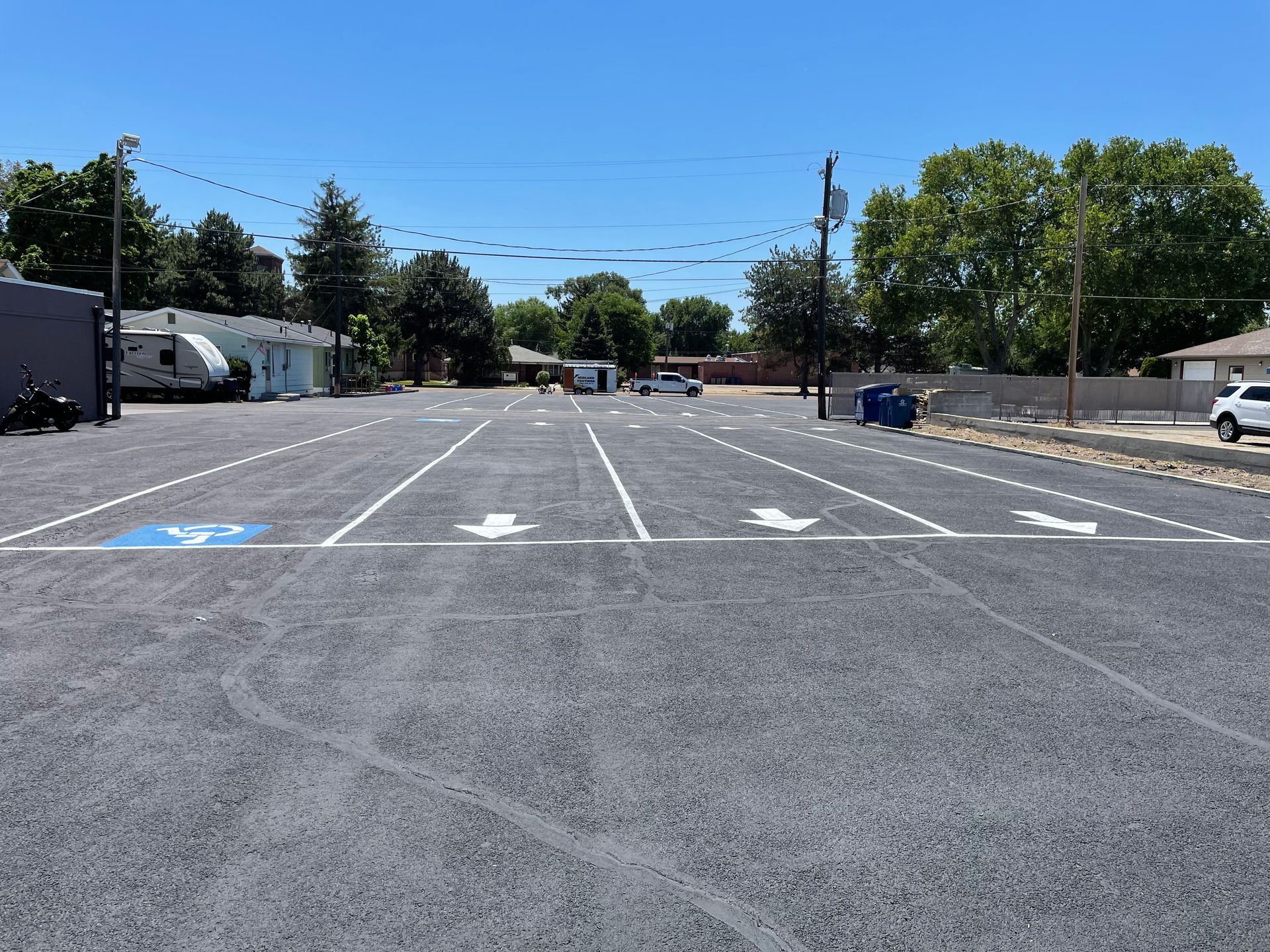 A newly paved parking lot with painted white parking lines, directional arrows, and a blue handicap-accessible space.
