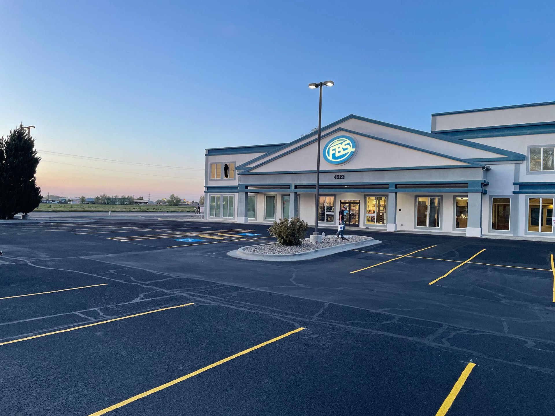 A commercial building with an F&S logo at sunset, featuring an empty parking lot with marked spaces in the foreground.