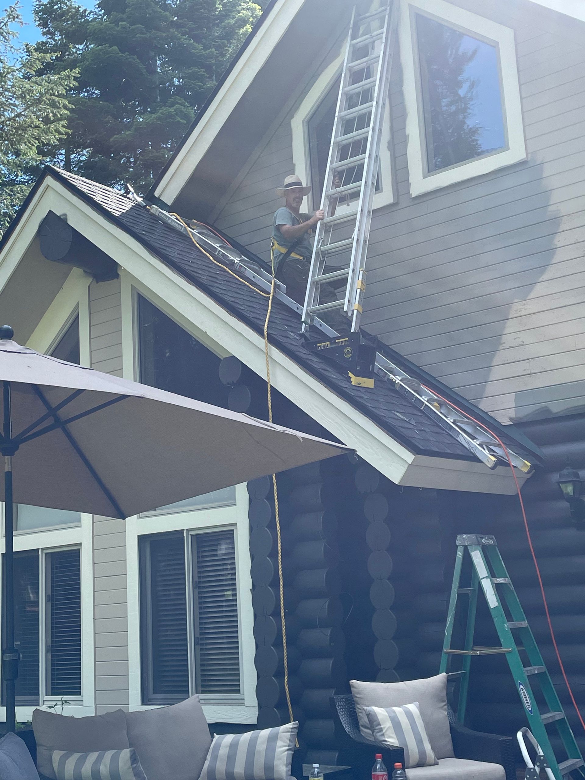 A person climbs an extension ladder resting on a slanted roof to reach a high window on a multi-story home.