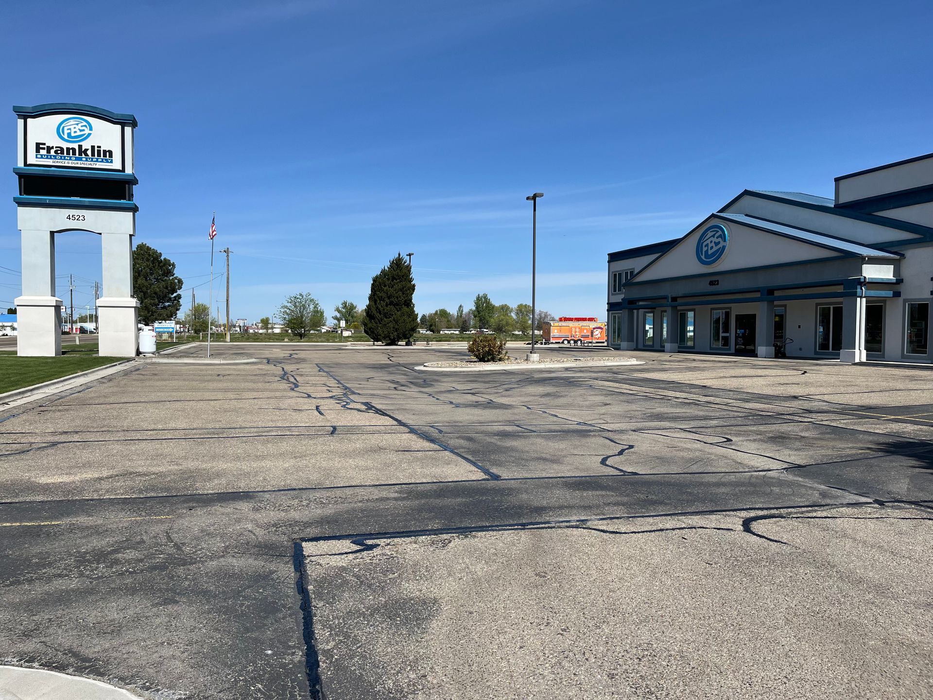 A large, empty parking lot in front of a blue and white building with a matching freestanding sign under a clear blue sky.