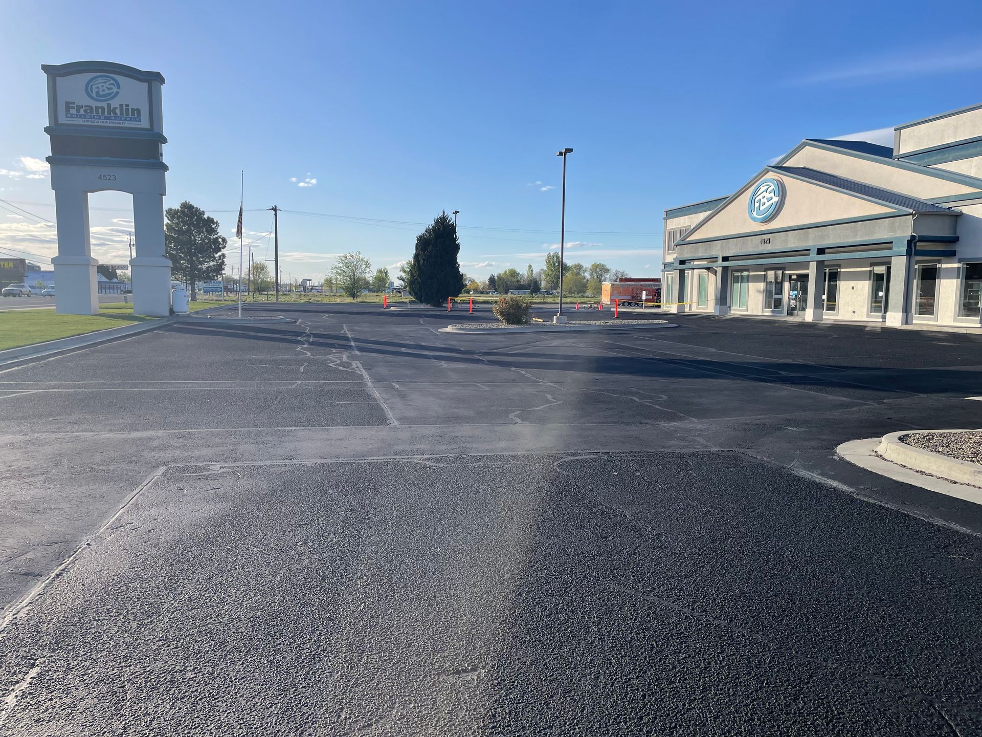 A newly paved parking lot at a building with a tall white entrance sign under a clear blue sky.