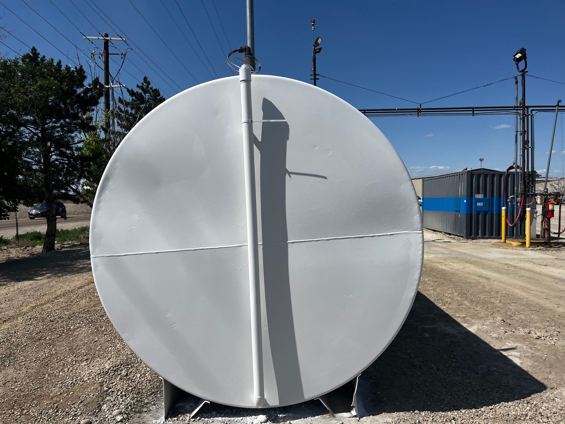 A white, cylindrical industrial storage tank positioned horizontally on a gravel surface outdoors.