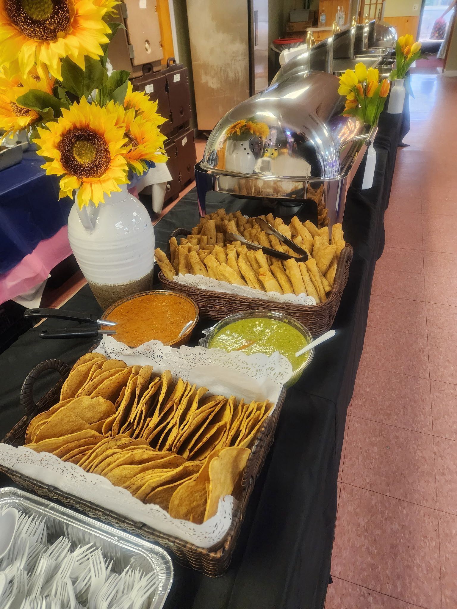 A buffet table with tortilla chips , dips , and sunflowers on it.