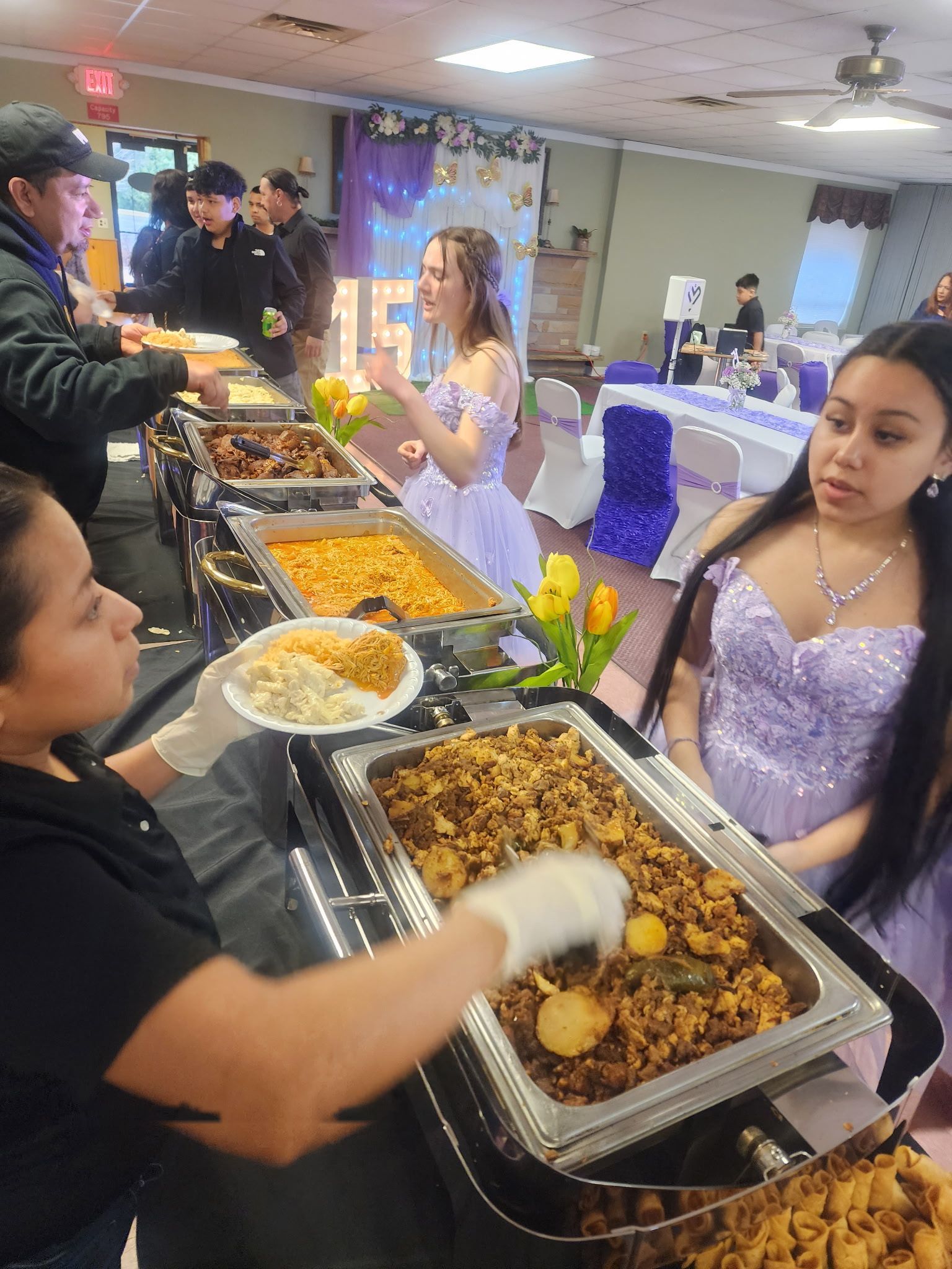 A woman in a purple dress is getting food from a buffet table.