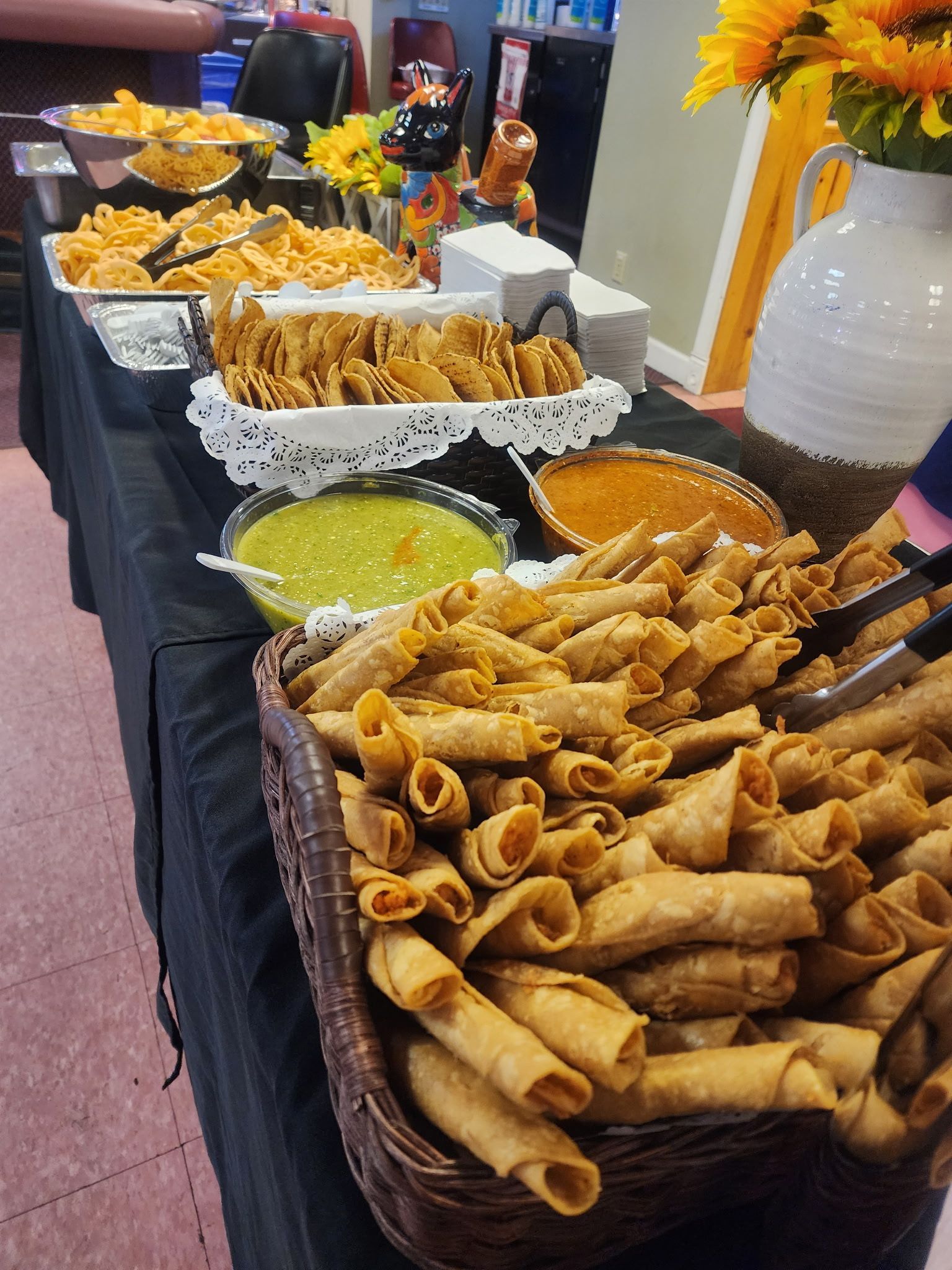 A buffet table with a variety of food including tacos and dips.