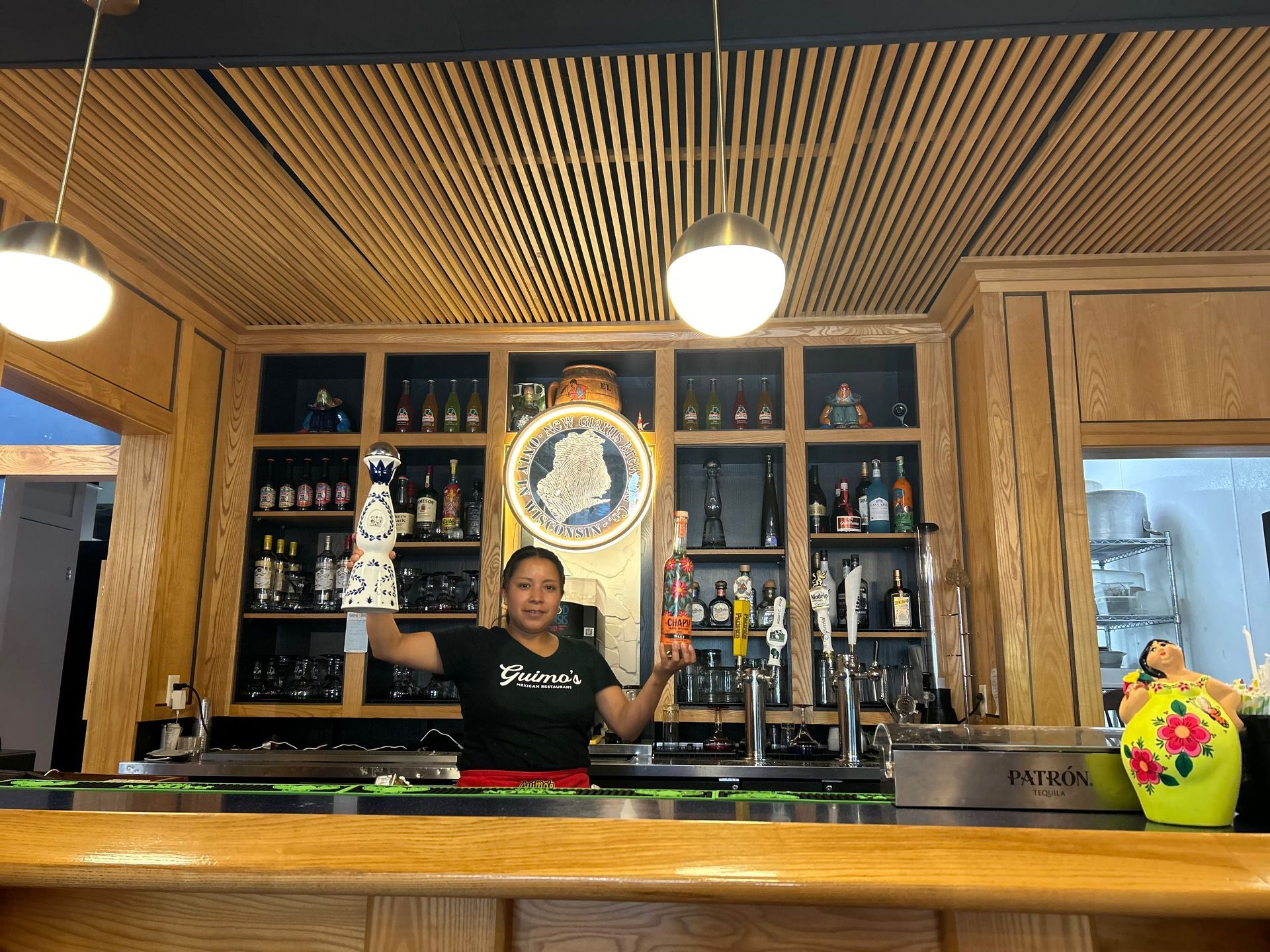 A woman is standing behind a bar holding a glass of wine.