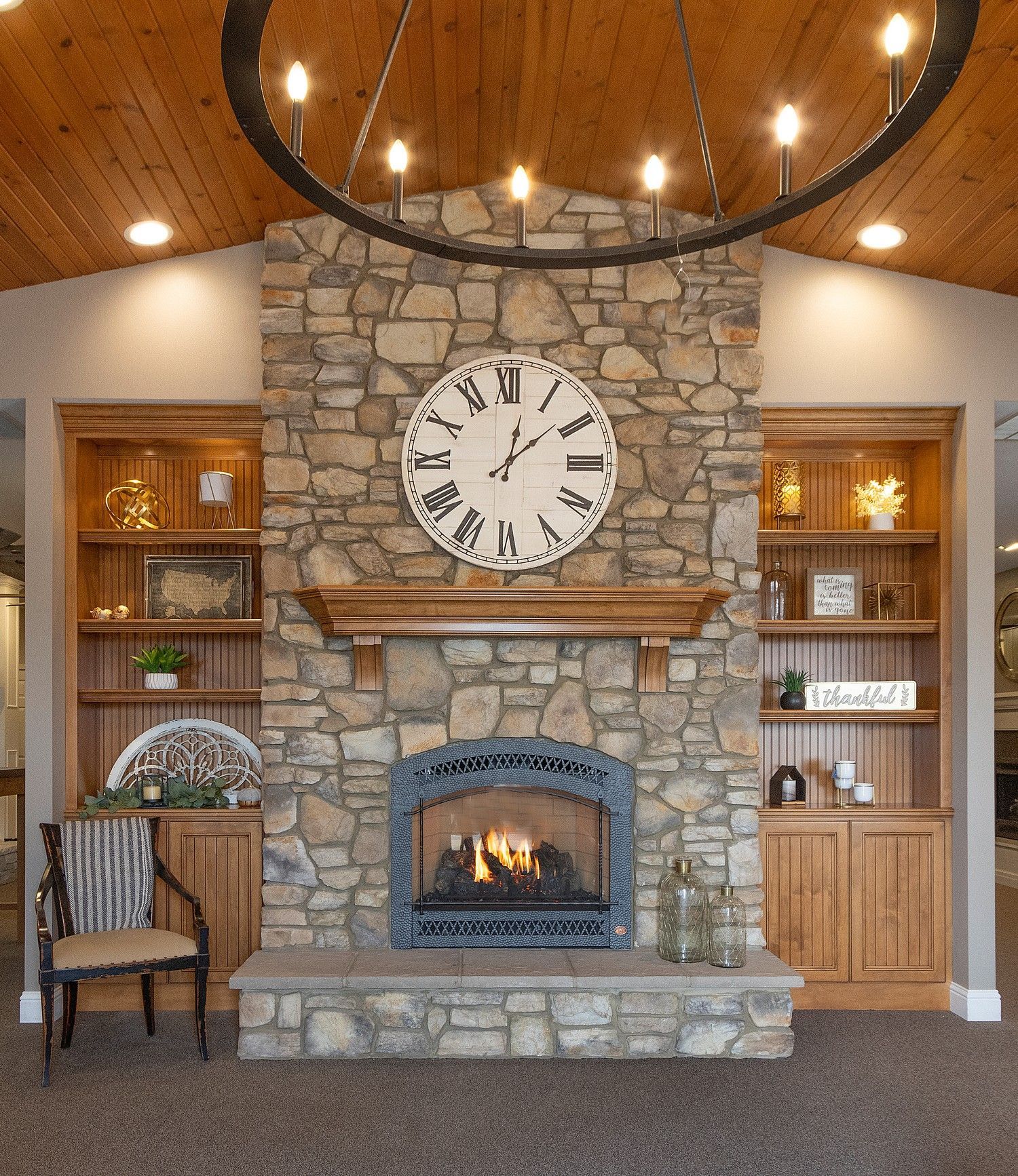 Rustic stone fireplace with large wall clock, built-in shelves, and a glowing fire in a cozy room