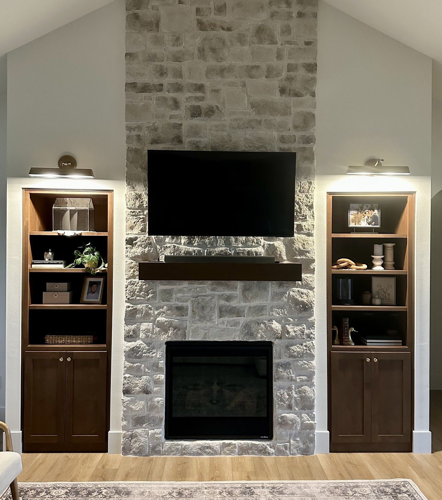 Stone fireplace wall with mounted TV, dark mantel, and matching built-in cabinets on both sides