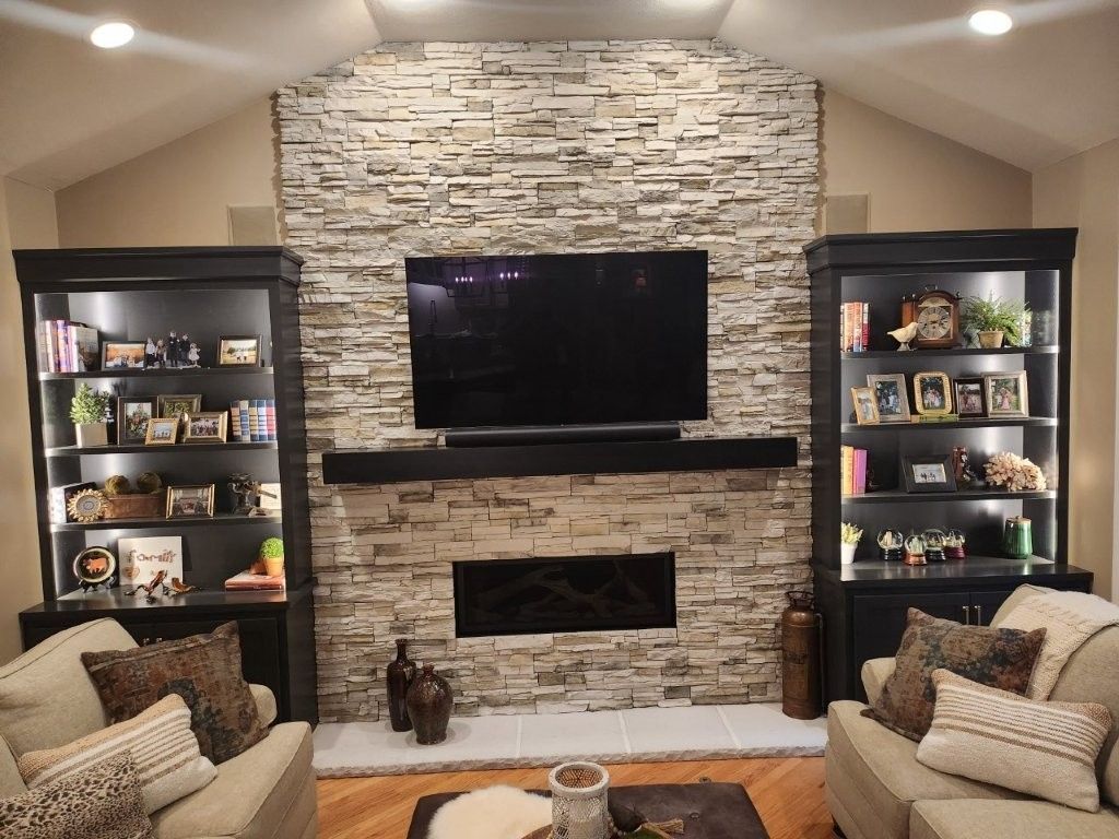 Living room with a stone fireplace, mounted TV, built-in shelves, and armchairs on either side.