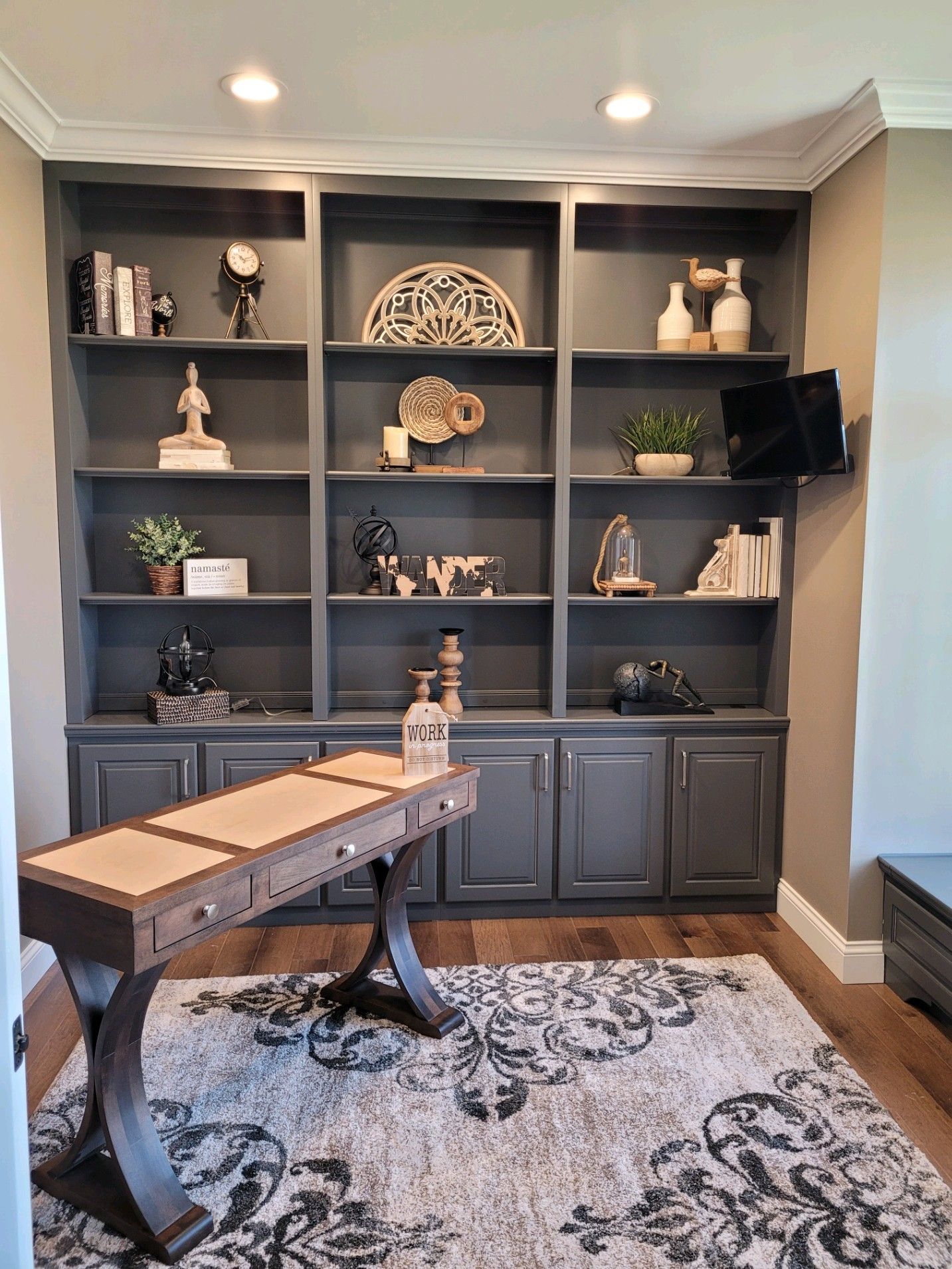 Home office with built-in dark shelving, decorative items, desk, and patterned rug