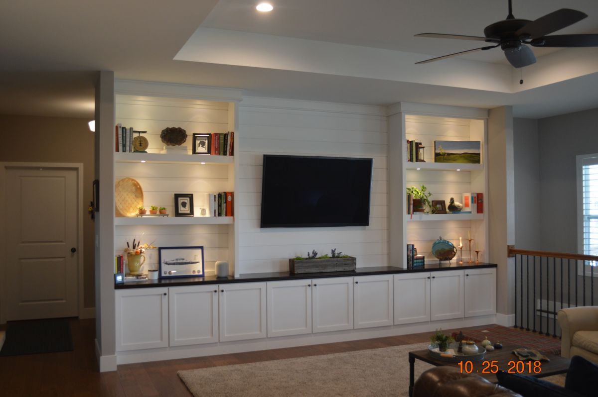 Living room with a wall-mounted TV, built-in white cabinets, shelves, and a ceiling fan