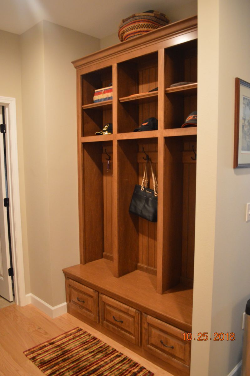 Wooden hallway built-in cubby bench with baskets and coat hooks beside a door, on a striped rug.