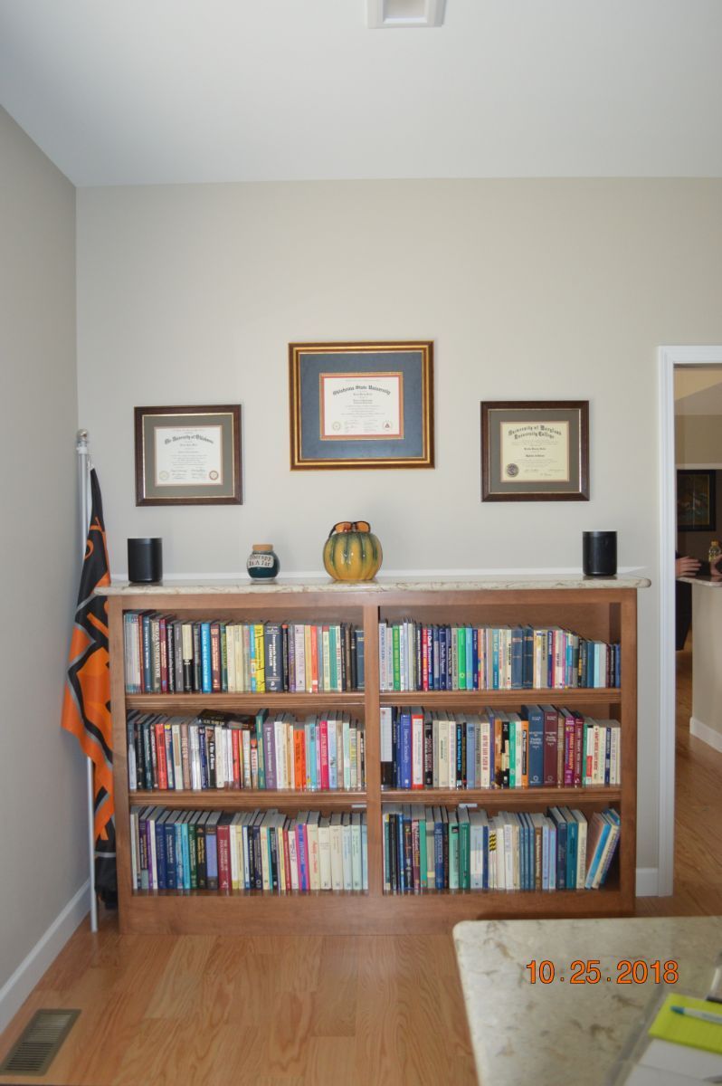 Bookshelf in a living room with framed wall art above and books and decor on top.