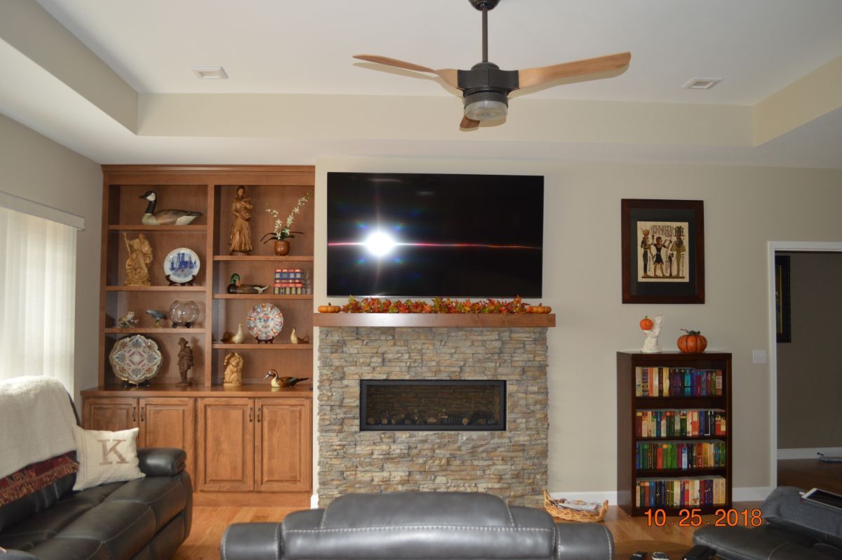 Living room with stone fireplace, large TV, wooden shelving, and ceiling fan
