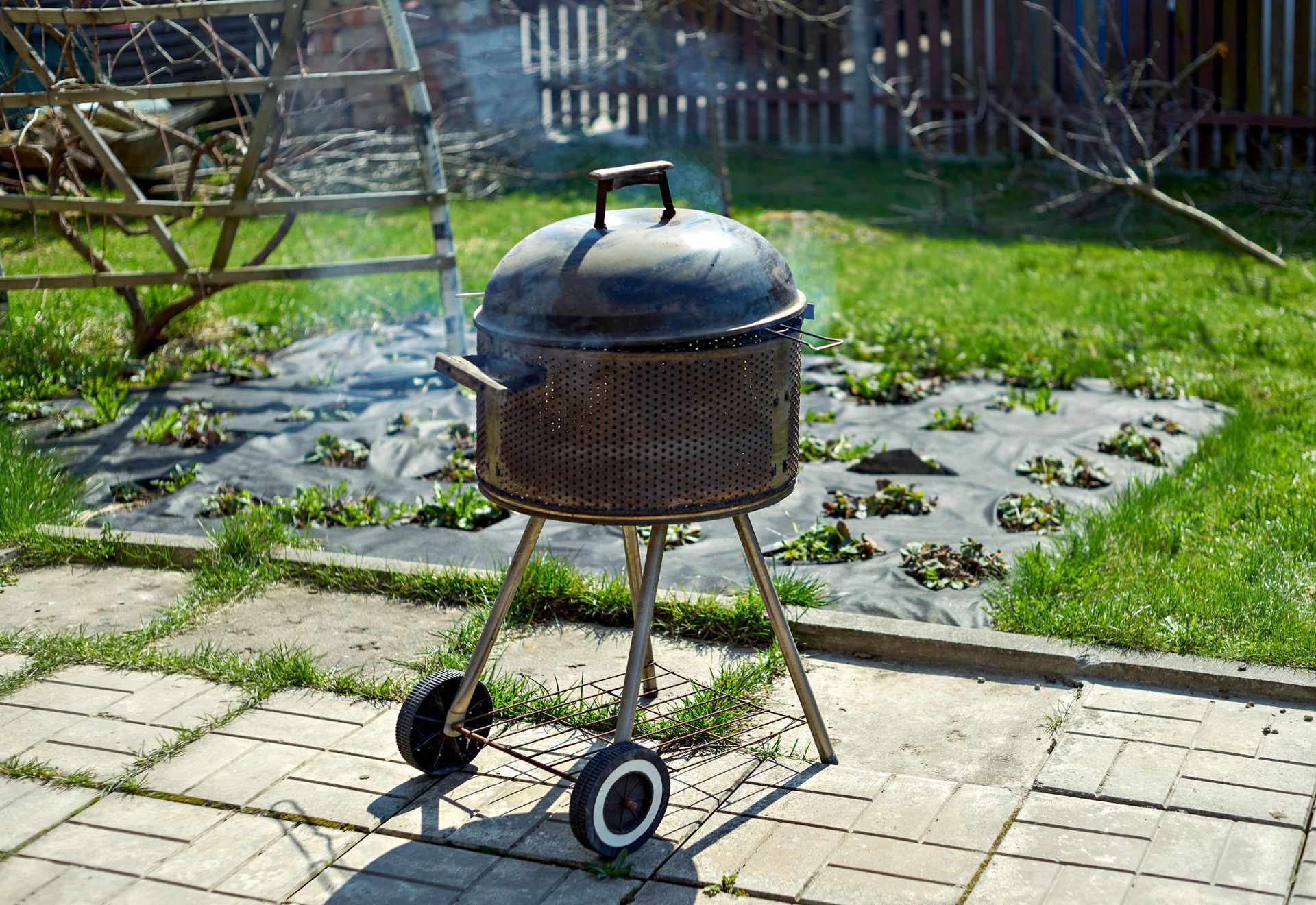 Round charcoal grill on wheels in a grassy backyard patio area