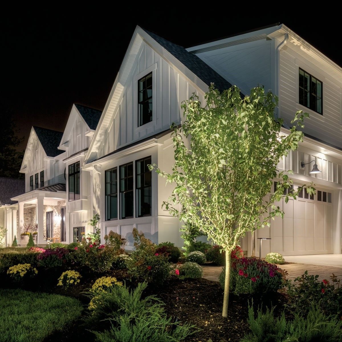 Illuminated white house with black trim and landscaped garden at night