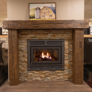 Stone fireplace with a lit gas insert and rustic wooden mantel in a room