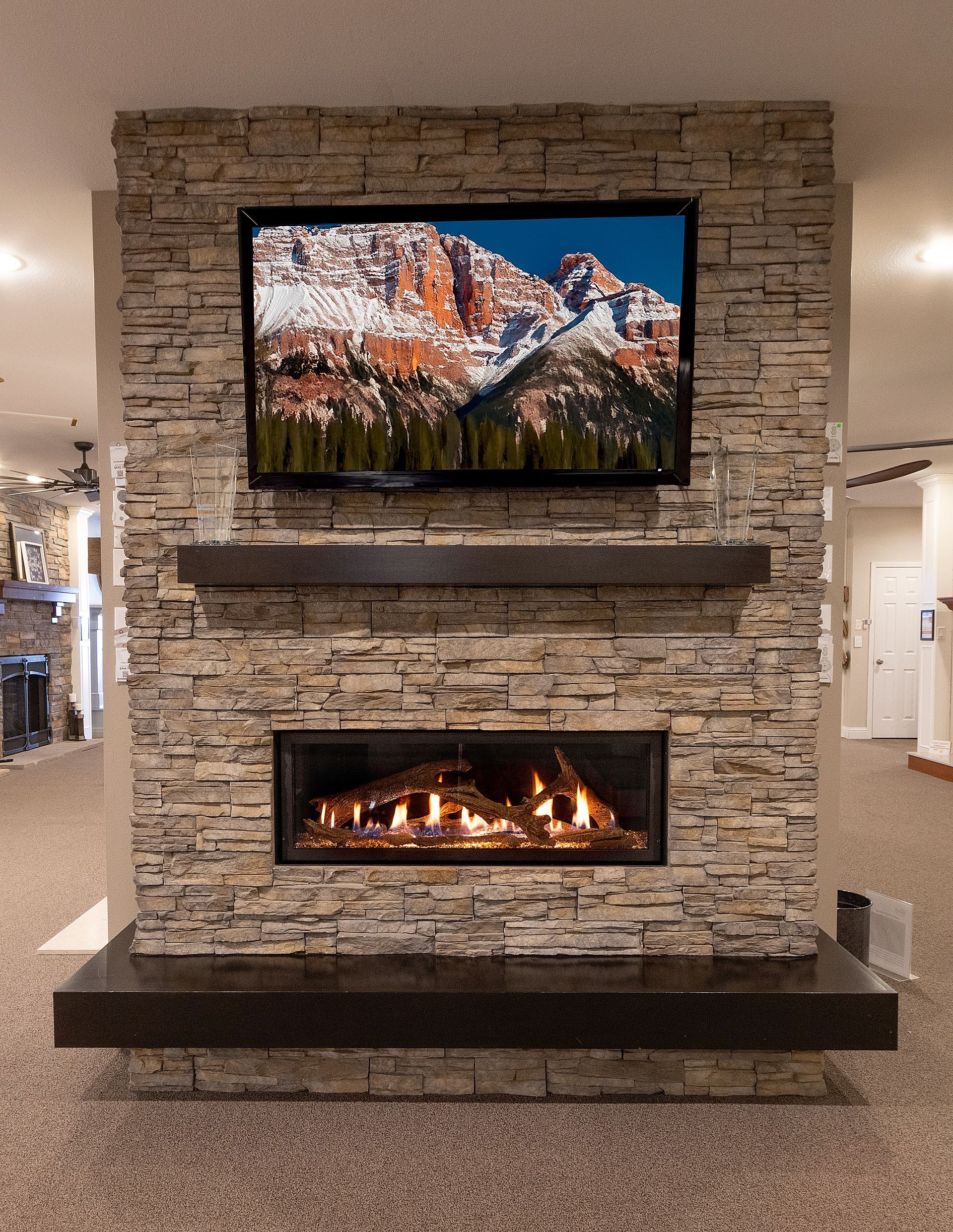 Stone fireplace display with a TV above and a lit electric fire below in a showroom setting