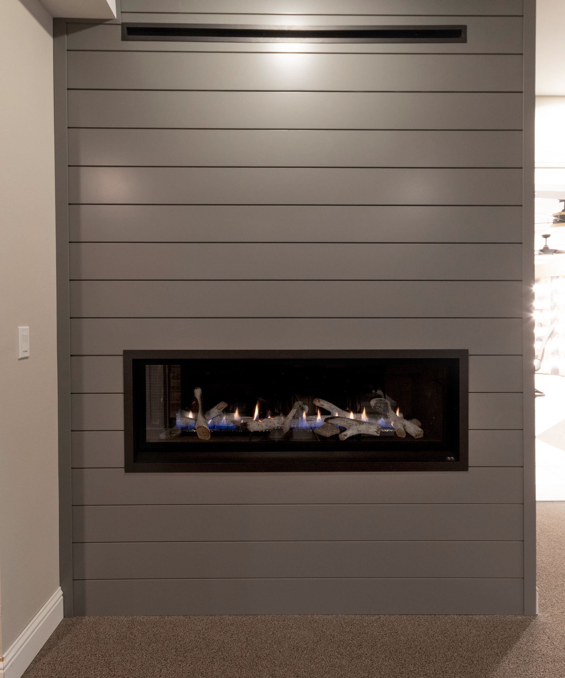 Modern gray wall with a long horizontal electric fireplace and narrow vent above it.