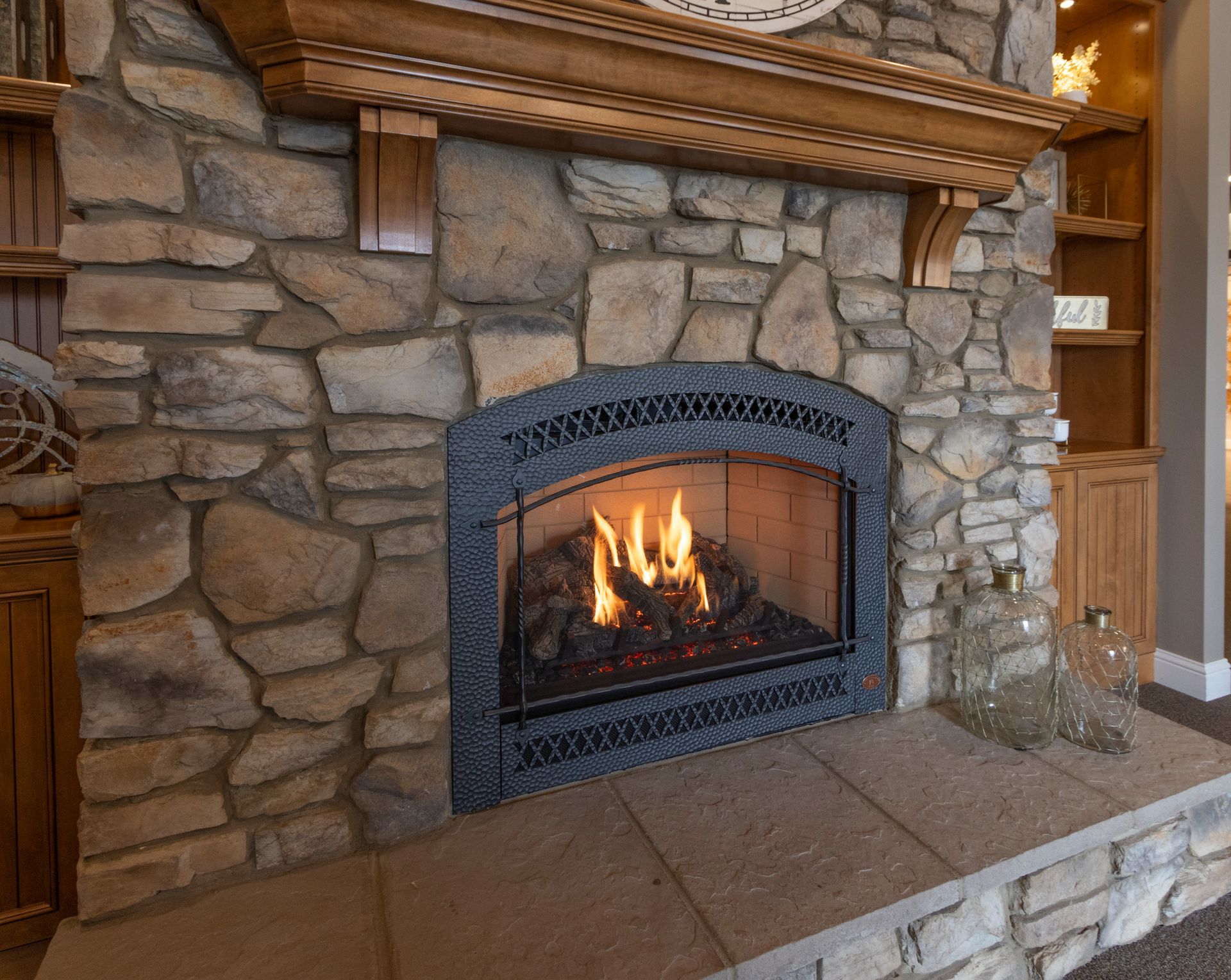 Stone fireplace with a lit fire, black iron surround, and rustic wood mantel in a cozy room