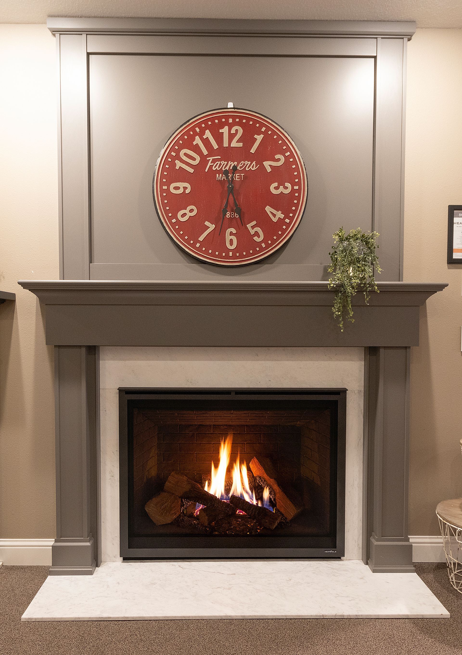 Living room fireplace with a fire, gray mantel, and large red wall clock above it