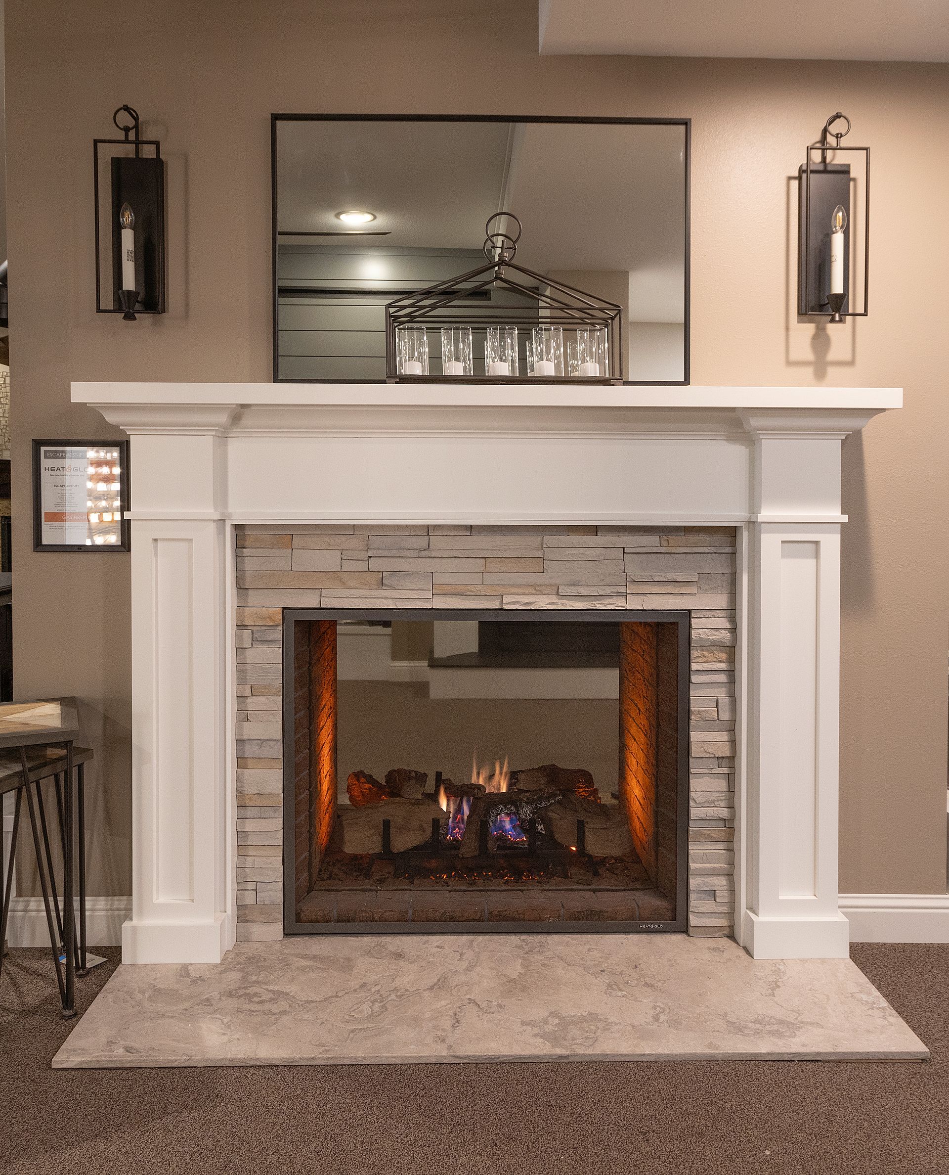 White fireplace with lit fire, mantel, mirror, and wall sconces in a beige living room.