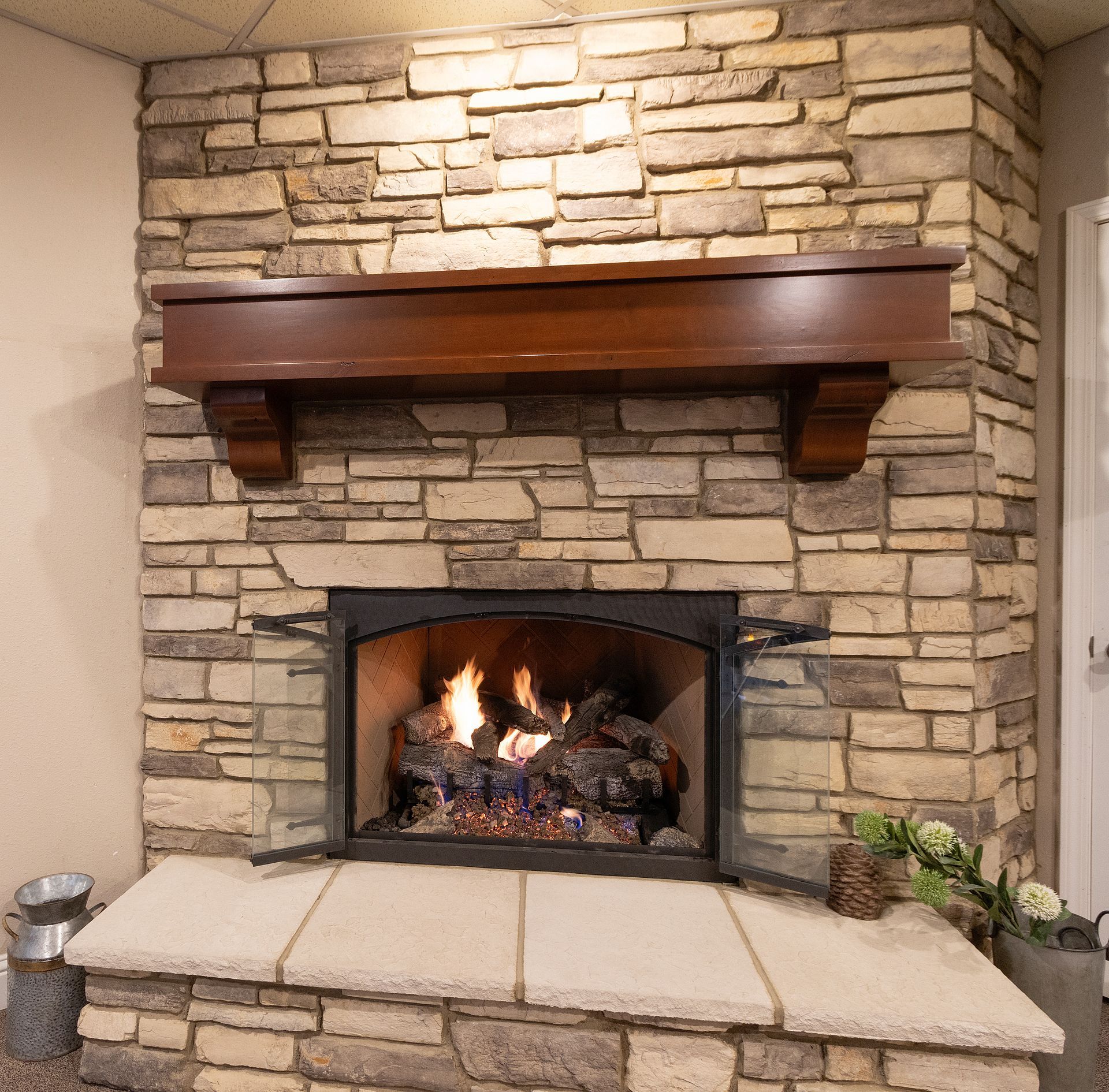 Stone fireplace with a lit fire, dark wood mantel, and beige hearth in a living room
