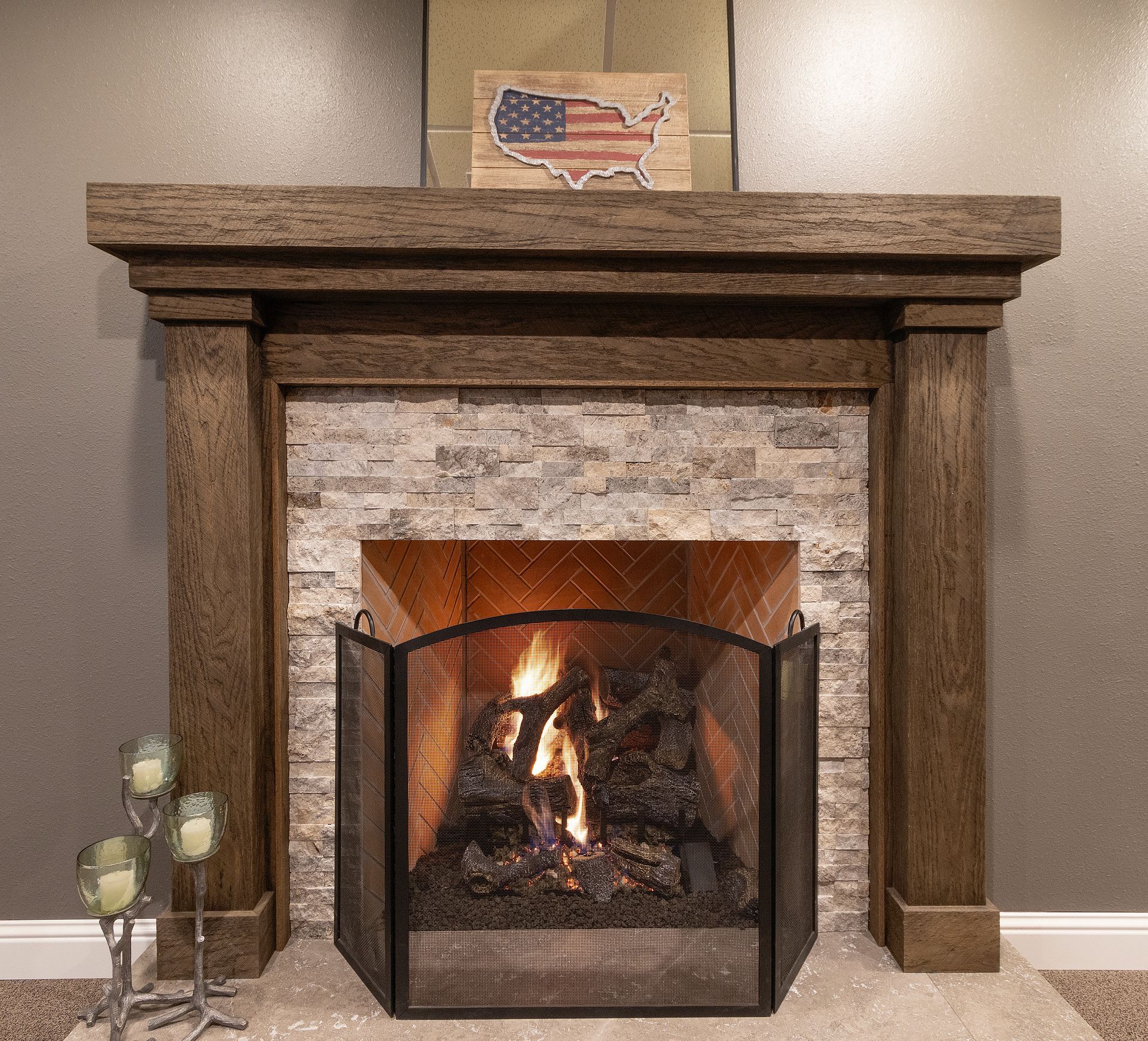 Stone fireplace with a burning fire, black screen, and a small American flag decoration on the mantel.