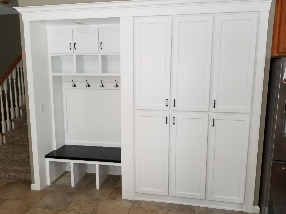 White built-in mudroom cabinet with hooks, bench, and tall storage cabinets on the right
