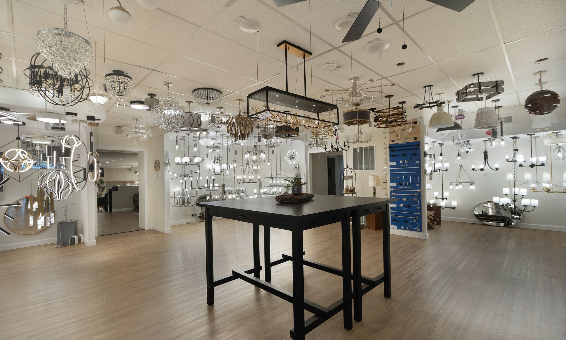 Modern lighting showroom with many hanging fixtures and a central black display table.