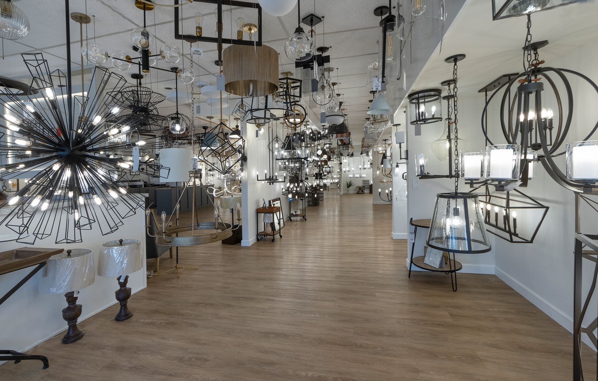 Lighting showroom with modern chandeliers, pendant lights, and floor lamps along a long display aisle