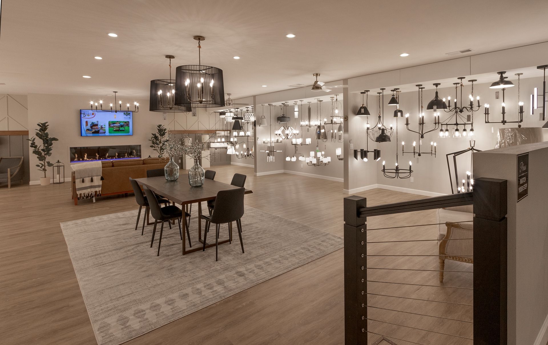 Modern showroom with dining table, chairs, and rows of hanging light fixtures displayed on white walls.