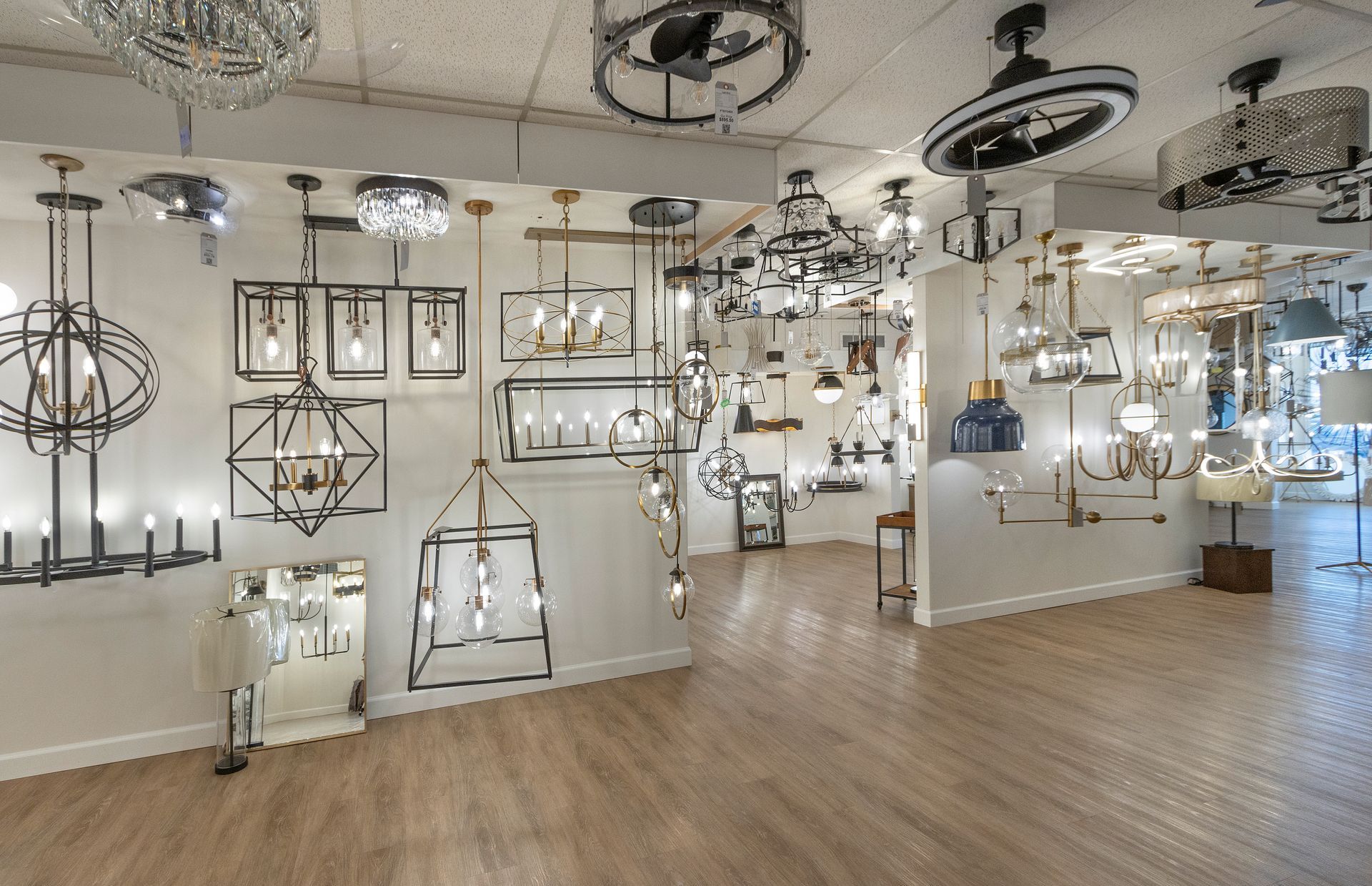 Bright showroom displaying many hanging light fixtures in a modern, white interior with wood flooring