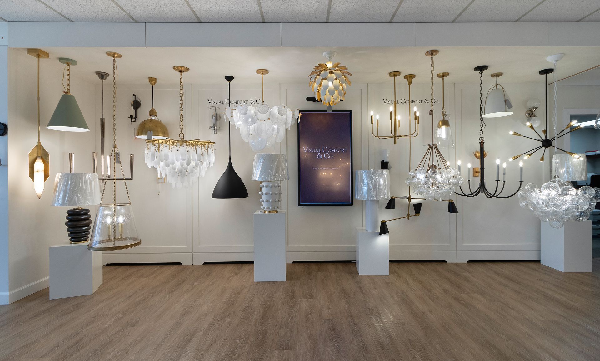 Elegant lighting showroom displaying assorted chandeliers and pendant lamps on white pedestals.