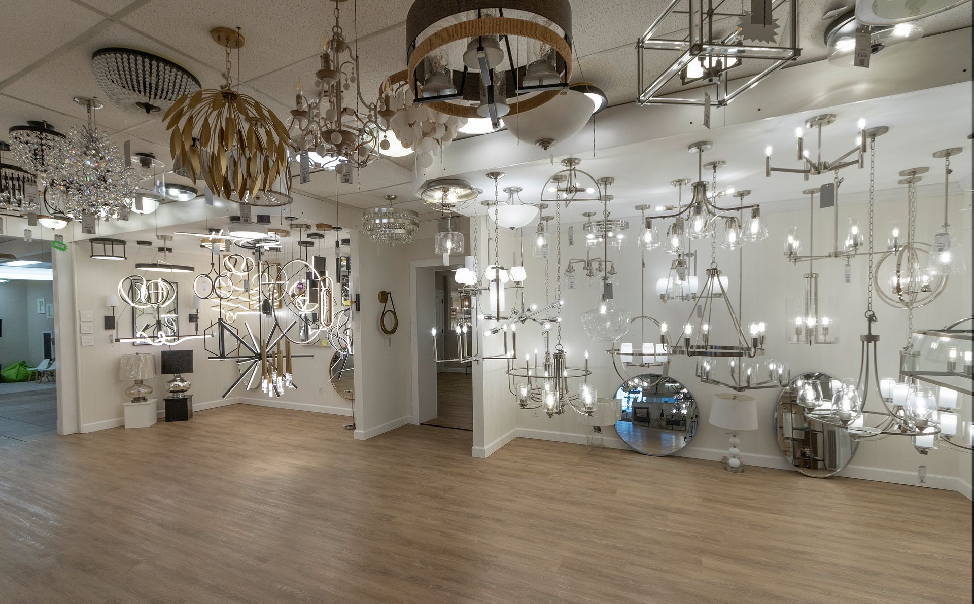 Modern lighting showroom with many hanging fixtures, mirrors, and a wood floor