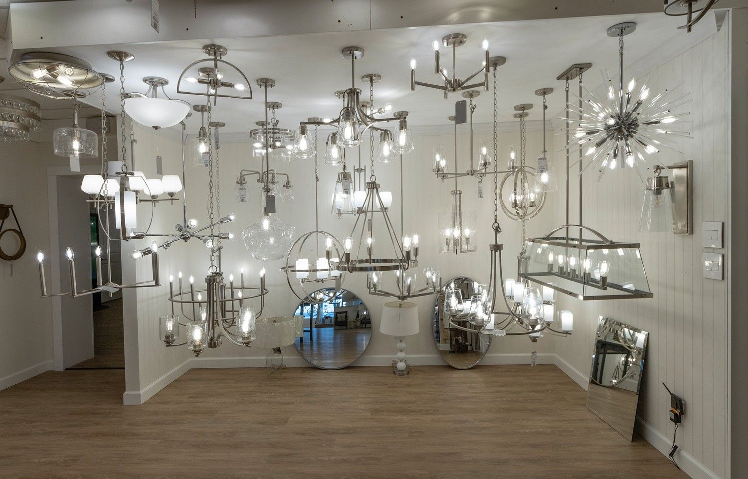 Large showroom filled with many hanging and wall-mounted chrome chandeliers in a bright room