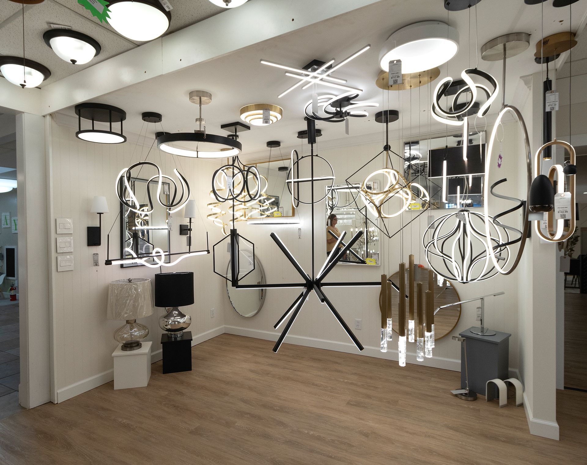 Modern lighting showroom with hanging ceiling fixtures, wall sconces, and floor lamps on display.