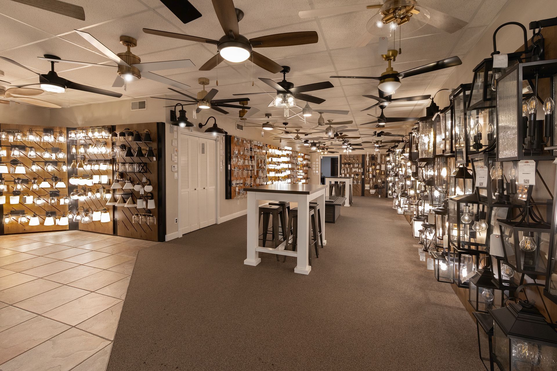 Indoor lighting showroom with ceiling fans, hanging fixtures, and display tables on a carpeted floor